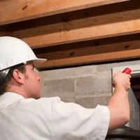 Termite inspection technician checking a basement wall and framing for termite activity in Erie, PA